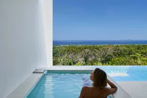 人物在現代極簡風格的泡湯池中放鬆，俯瞰茂密綠意與海洋景色。