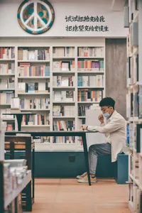 A man in a bookstore reading area, sitting at a concrete table with a peace symbol and Chinese characters above him.