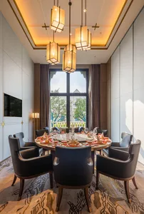 An industrial dining room featuring a large round table surrounded by black chairs, set with red and white tableware on a pat