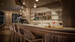 A modern bar with marble and wooden decor, featuring a well-stocked bar counter, chairs, and hanging lights.