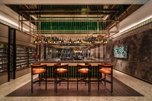 Modern bar with marble and glass materials, featuring metal railings and a variety of bottles.
