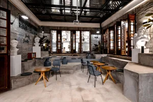 Modern coffee shop with concrete walls, wooden tables, and grey chairs.