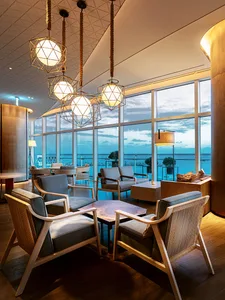 A contemporary hotel lobby with wooden furniture, geometric lighting, and a view of the ocean.