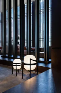 A modern hotel lobby with glass columns and light fixtures, featuring decorative vases on a wooden floor.
