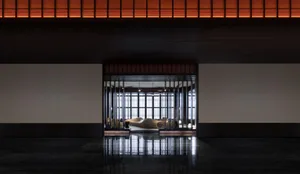 Interior view of a modern hotel lobby featuring wooden benches, glass walls, and metallic accents.