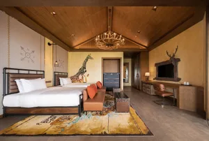 Modern hotel room featuring wood-themed decor and furniture, including a bed, sofa, desk, and chandelier.