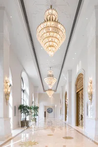 A grand, white corridor adorned with luxurious marble walls and illuminated by elegant glass chandeliers in a hotel setting.
