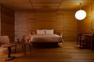 Minimalist bedroom with wooden furniture, a large bed, and a hanging light fixture.