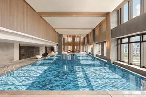 Modern minimalist indoor swimming pool with blue tiled floor, glass doors, and concrete walls