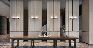 A modern lobby features a long wooden table with metal legs, adorned with a glass water feature, set against a backdrop of ma