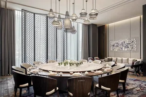 A modern dining room featuring a large, round marble table surrounded by high-backed chairs, with pendant lights hanging abov