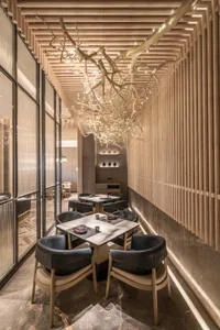 A modern restaurant interior featuring wooden chairs and tables with a distinctive chandelier.