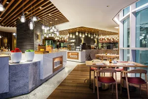 A modern restaurant interior with marble tables, wooden chairs, and glass lighting fixtures.