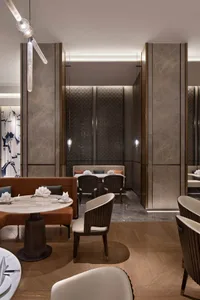 A modern restaurant with a seating area featuring marble tables, white leather chairs, and wooden floors.