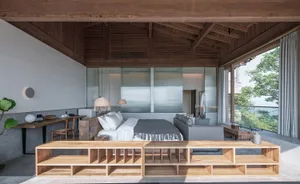 A minimalist bedroom with wooden furniture and concrete walls, featuring a large bed and a desk.