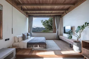 A modern, minimalist bedroom with a wooden platform bed, large window overlooking mountains, and minimalist decor.