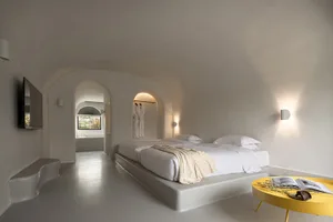 A minimalist bedroom with a concrete platform bed, white bedding, and yellow accents.