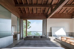 A modern bedroom featuring a bed with a wooden frame and a large window overlooking greenery.