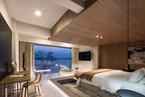A modern bedroom featuring a large window with a view of a tree, wooden walls, glass doors, and marble floors.