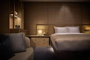 A modern bedroom featuring wooden paneling, white bedding, and a cozy seating area.
