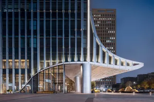 Modern building exterior with glass walls, concrete columns, and an aluminum awning.