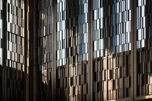 A close-up view of a modern building's glass façade, showing geometric patterns and reflections.