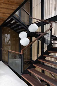 A modern staircase with wooden steps, black railings, and white spherical lanterns hanging from the ceiling.