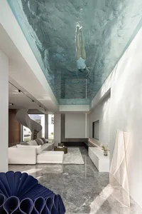 A modern living room with a glass ceiling and a person swimming underwater.