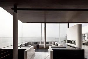 Minimalist living room with marble and concrete materials featuring a large sectional sofa and a panoramic view of the water.