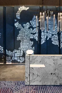 A modern lobby featuring a marble wall with a map pattern, ambient lighting, and geometric hanging lights.