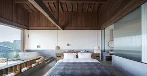 Spacious bedroom with minimalist design, featuring a large bed, wooden floor, and large windows.