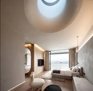 Modern minimalist bedroom featuring wooden furnishings and a circular skylight overlooking a body of water.