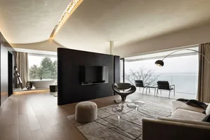 A modern minimalist living room with glass terraces overlooking a serene body of water.