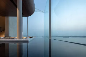 A modern residential space featuring large glass windows overlooking a serene water view.