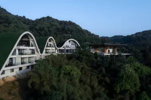 A modern residential resort with curved concrete structures amidst a lush, green forested area.