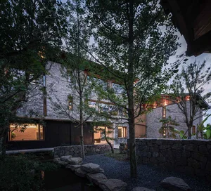 Modern residential house with stone exterior surrounded by greenery at dusk.