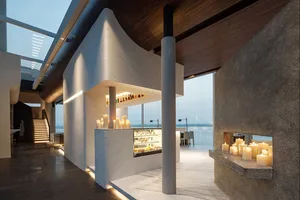 Modern rooftop restaurant with concrete and marble finishes, featuring a bar area with candles.