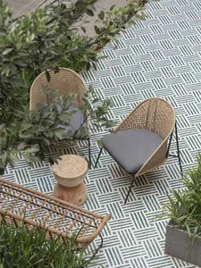 Two wicker chairs with gray cushions placed on a patterned marble tile floor outdoors.