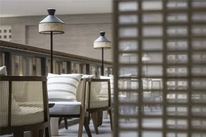Modern restaurant bar with wooden cane seating and textile cushions, featuring sleek floor lamps with woven shades.