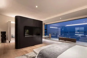 Modern bedroom with a black accent wall, a white bed, and a large glass window overlooking the ocean.