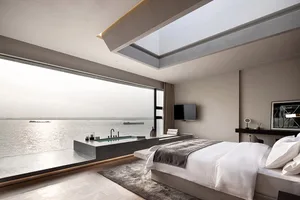 A modern minimalist bedroom featuring a concrete bathtub with a view of the water and a large window allowing natural light t