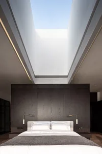 A minimalist bedroom with a double bed, dark wooden headboard, and skylight allowing natural light in.