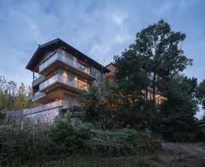 A modern residential building with stone exterior and wooden elements, illuminated at dusk.