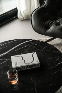 A marble coffee table with a book titled 'Alvar Aalto' and a glass of drink.