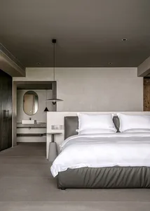 A minimalist bedroom with concrete walls, flooring, and a bed with white bedding.
