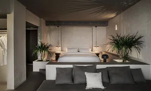 An image of a minimalist bedroom featuring a concrete bed platform and floating nightstands with leafy green indoor plants, a