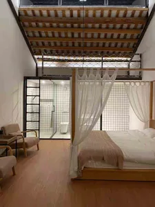 Modern bedroom interior with wooden flooring, bed with sheer curtains, and white tiled bathroom in the background.