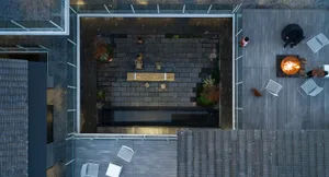 Aerial view of a modern concrete patio featuring a glass fireplace, outdoor seating, and landscaping.