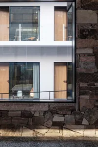 An exterior view of a modern building featuring stone walls and large glass windows.