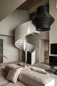 A modern minimalist living room features a white spiral staircase and a large black wicker lamp hanging above a comfortable s